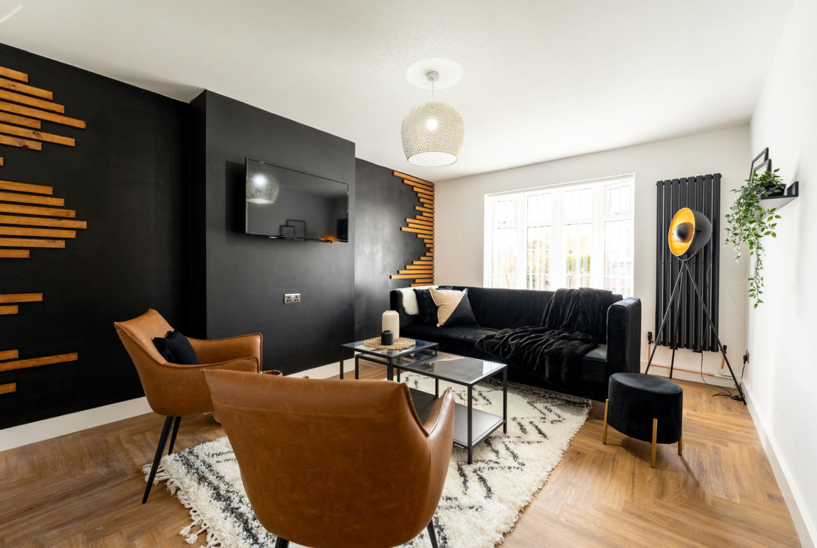 TV lounge with light brown leather chairs and having black velvet sofa in the property of link road by hmh stays