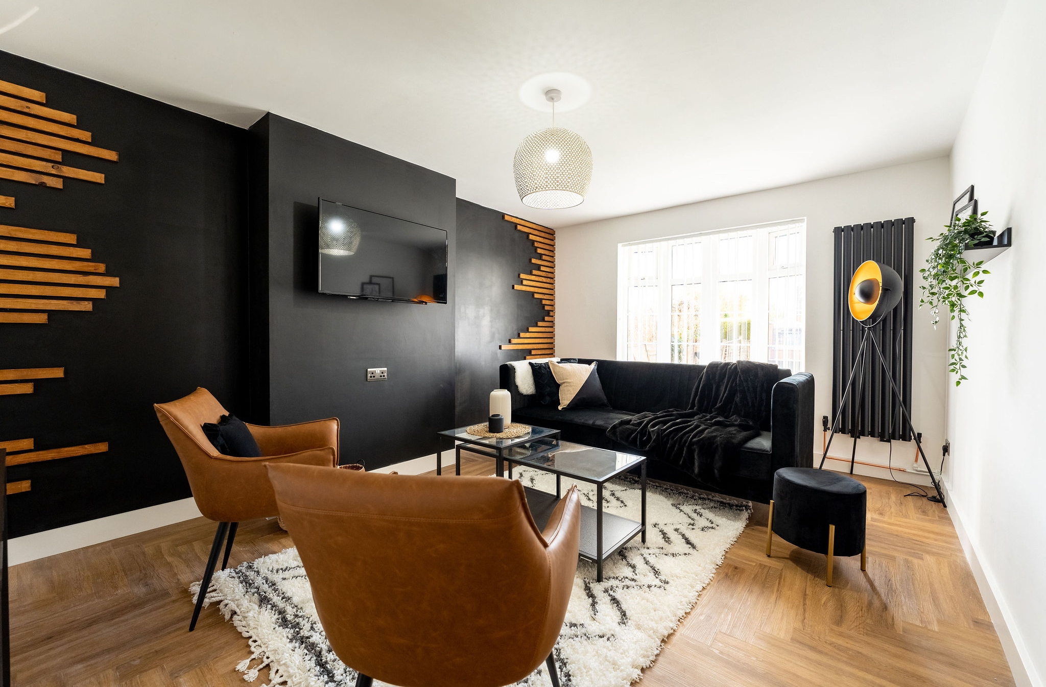 TV lounge with light brown leather chairs and having black velvet sofa in the property of link road by hmh stays